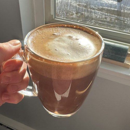 hand holding cup of maple mocha latte with the sun shining in the window