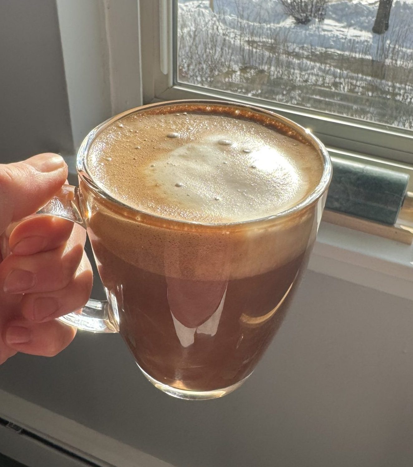 hand holding cup of maple mocha latte with the sun shining in the window