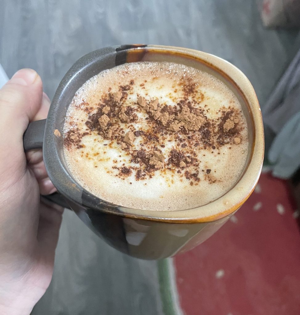 Hand holding hot cup of maple mocha latte with cocoa and cinnamon topping